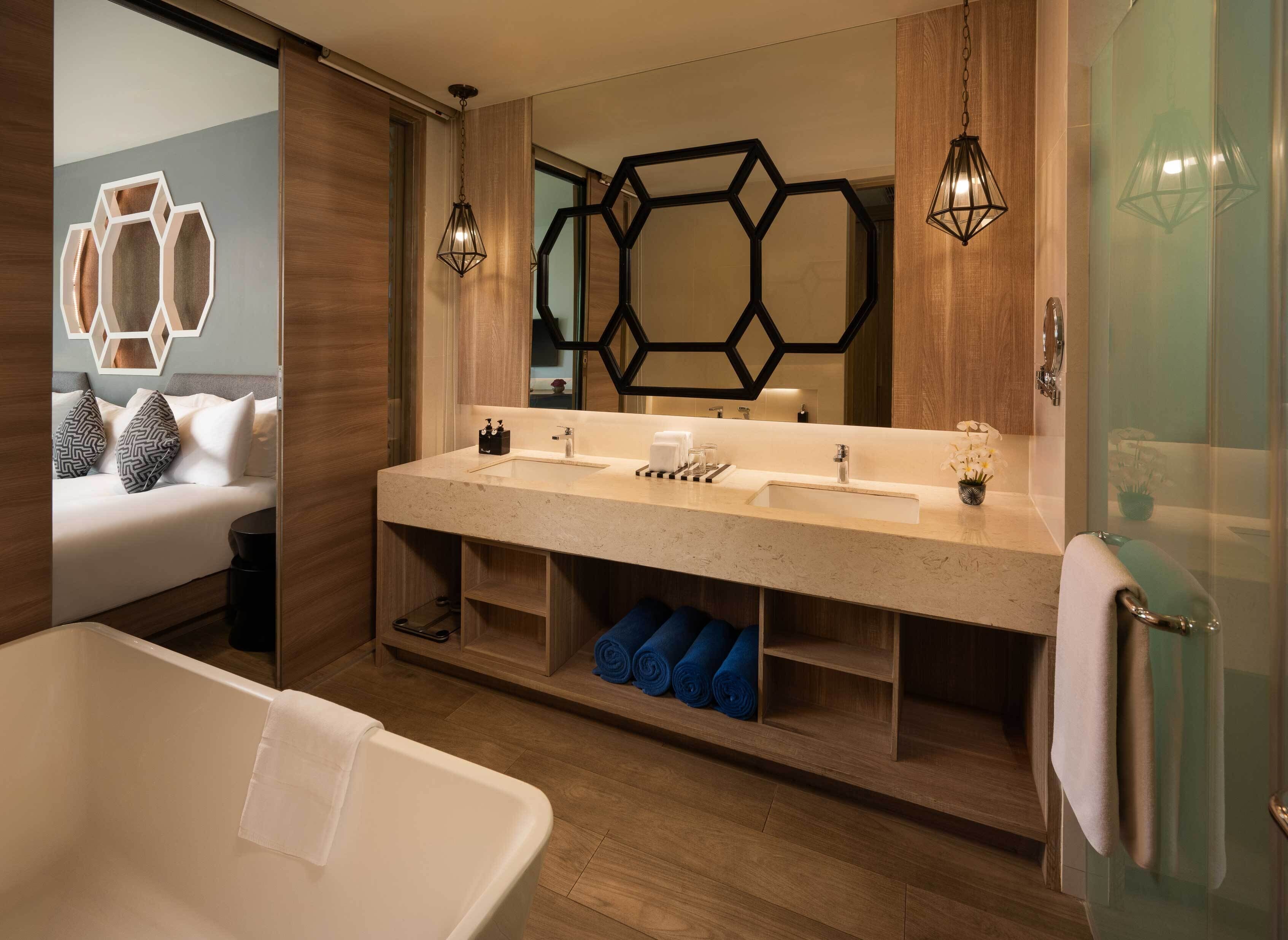 A modern bathroom with a large mirror, two pendant lights, a bathtub, and a vanity with a sink and towel rack.