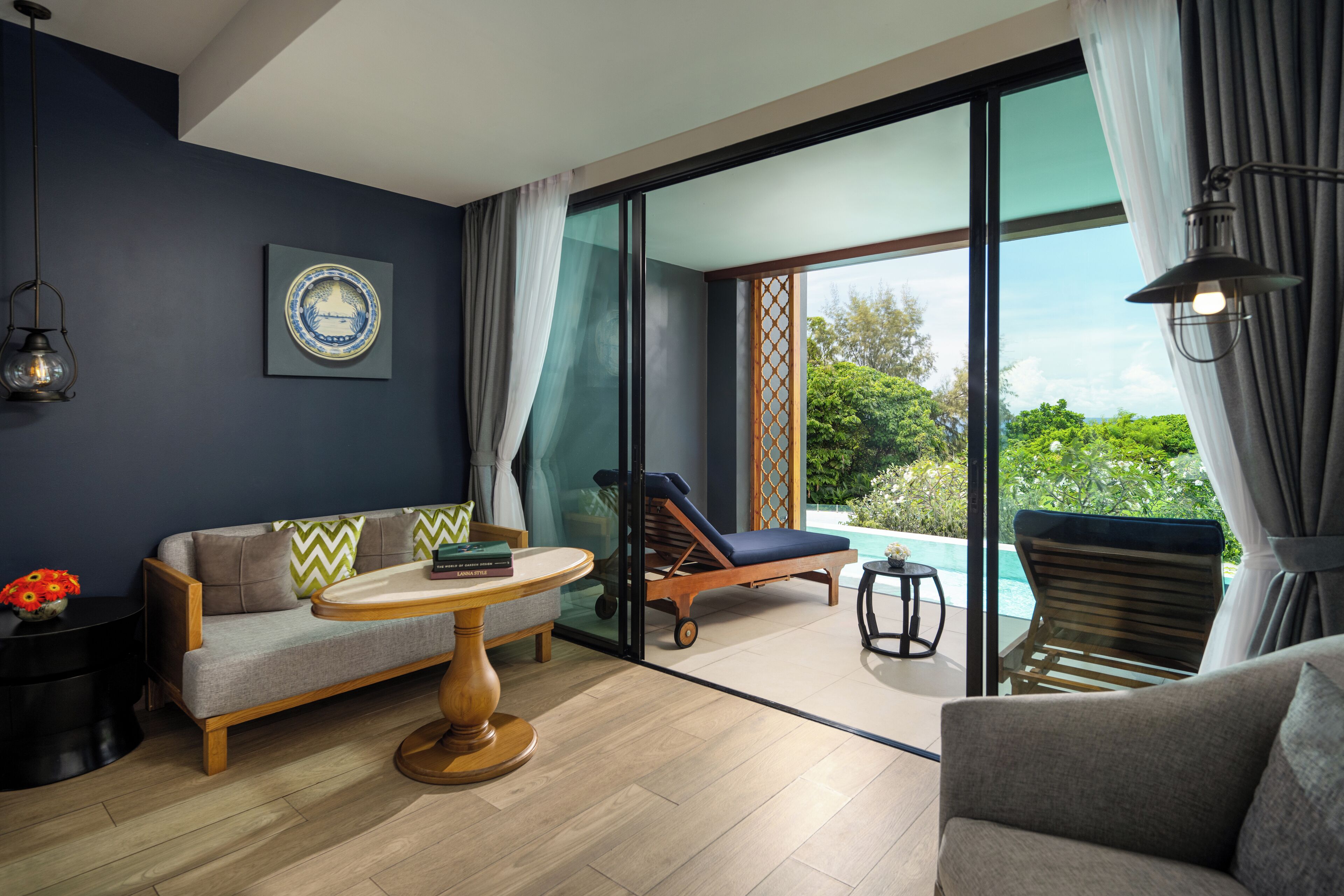 A modern living room with a sofa, a round table, and a lounge chair by a glass door leading to a pool.