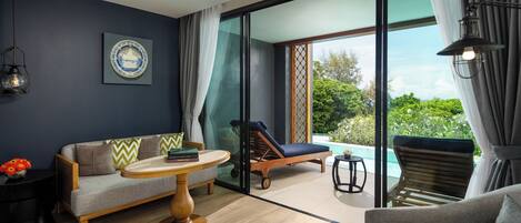 A modern living room with a sofa, a round table, and a lounge chair by a glass door leading to a pool.