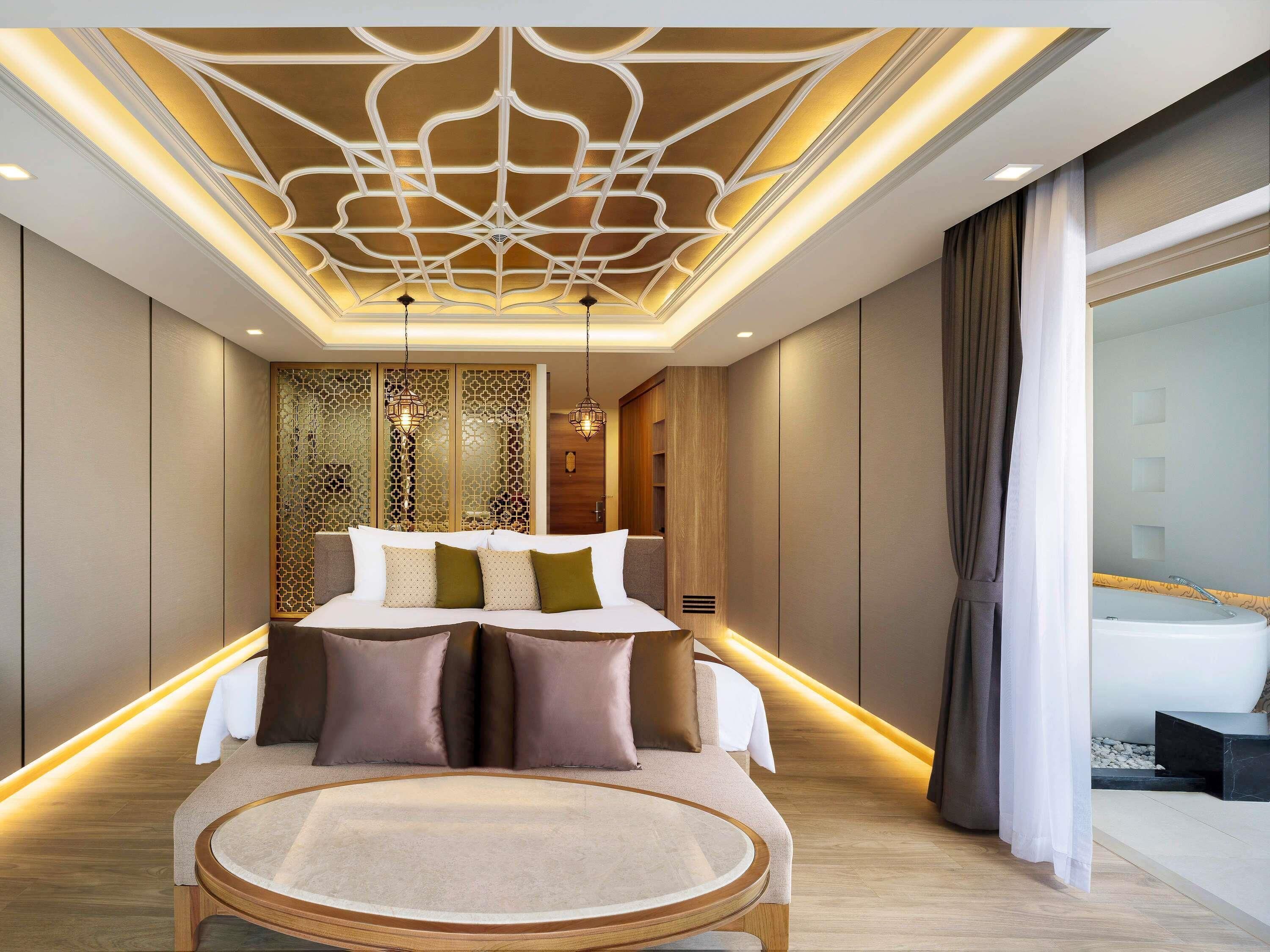 A modern bedroom with a bed, bedside tables, a round table, and a decorative ceiling.