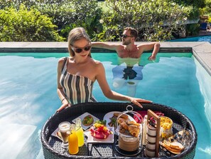 A poolside breakfast setup with a tray of food and drinks, surrounded by lush greenery. - Avista Grande Phuket Karon - MGallery (Karon)