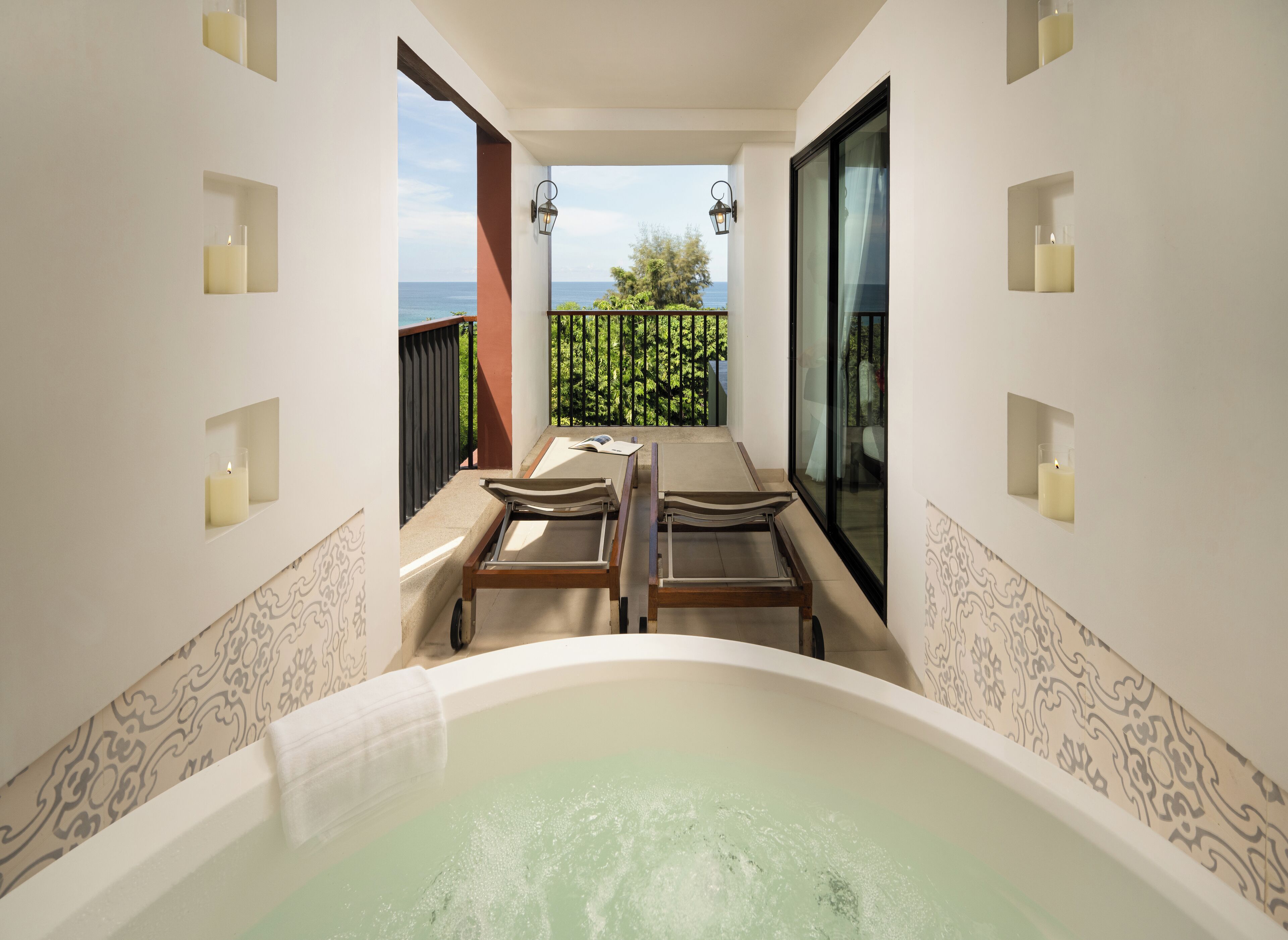 Un área de spa con un jacuzzi, dos tumbonas de madera y vistas al mar.