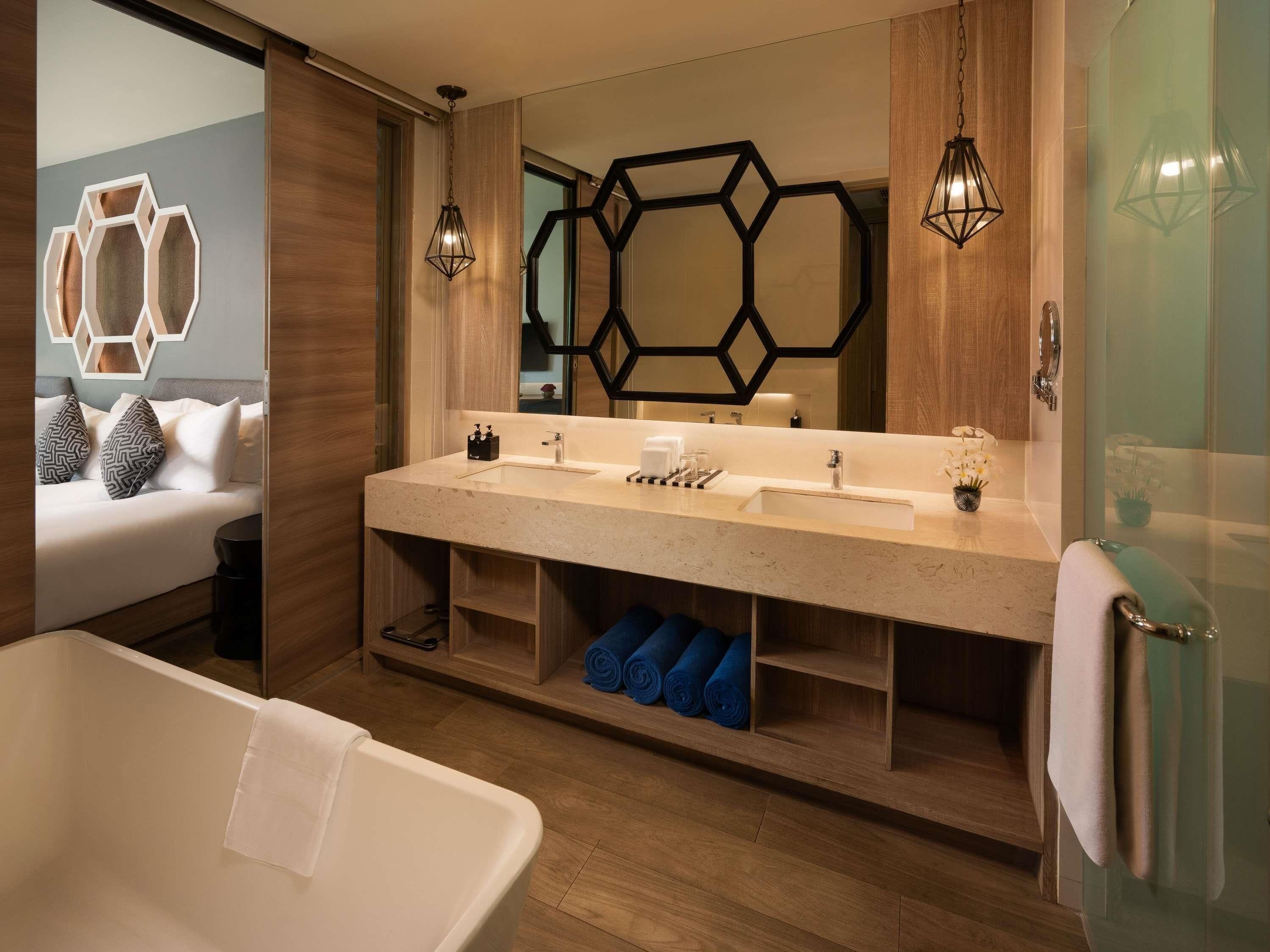 Une salle de bain moderne dotée d’une grande baignoire, d’un meuble-lavabo à deux vasques et d’un grand miroir agrémenté de motifs géométriques sur le mur.