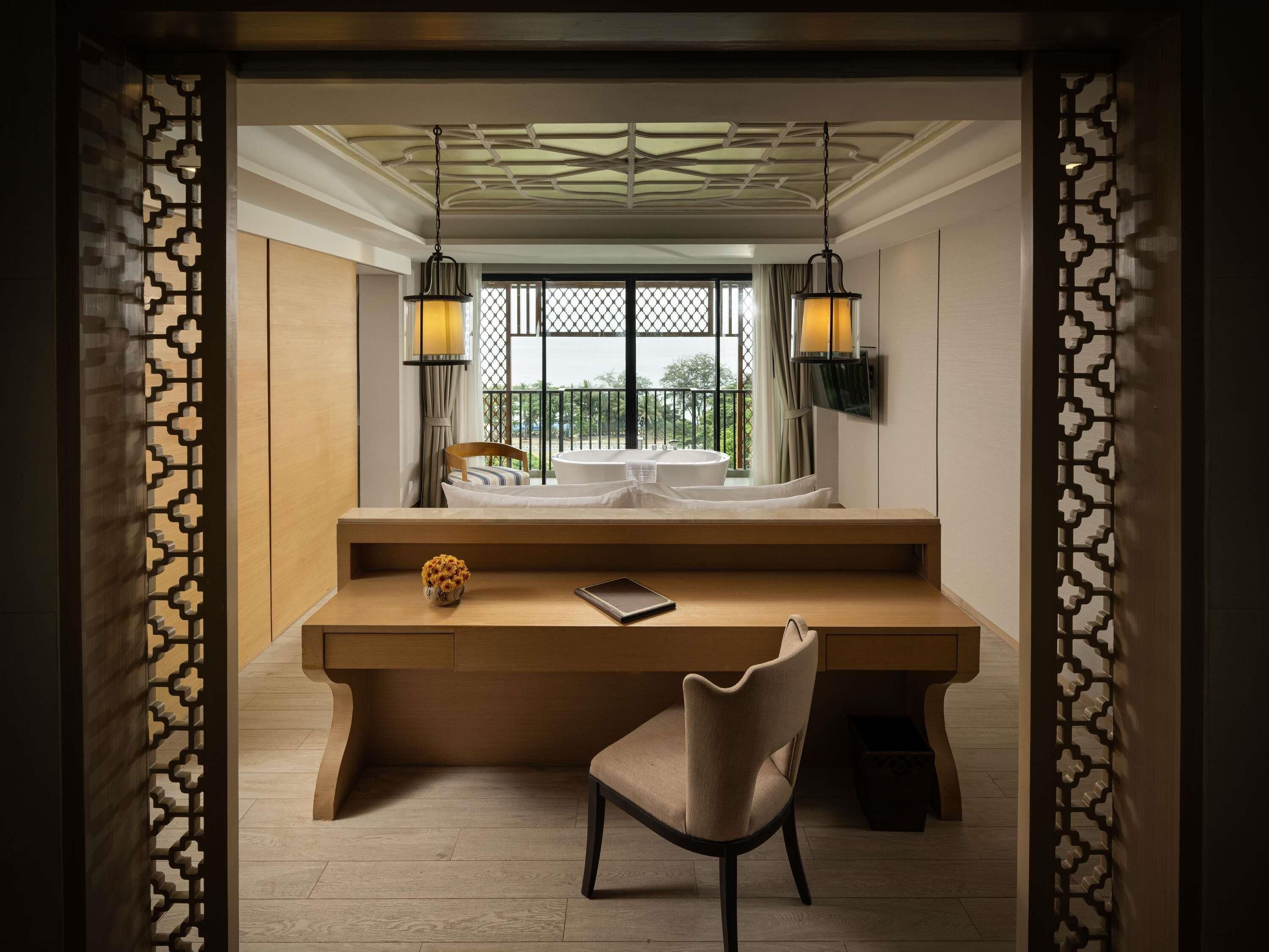 A room with a wooden desk, a chair, a bed with a view, and two wall-mounted lamps.