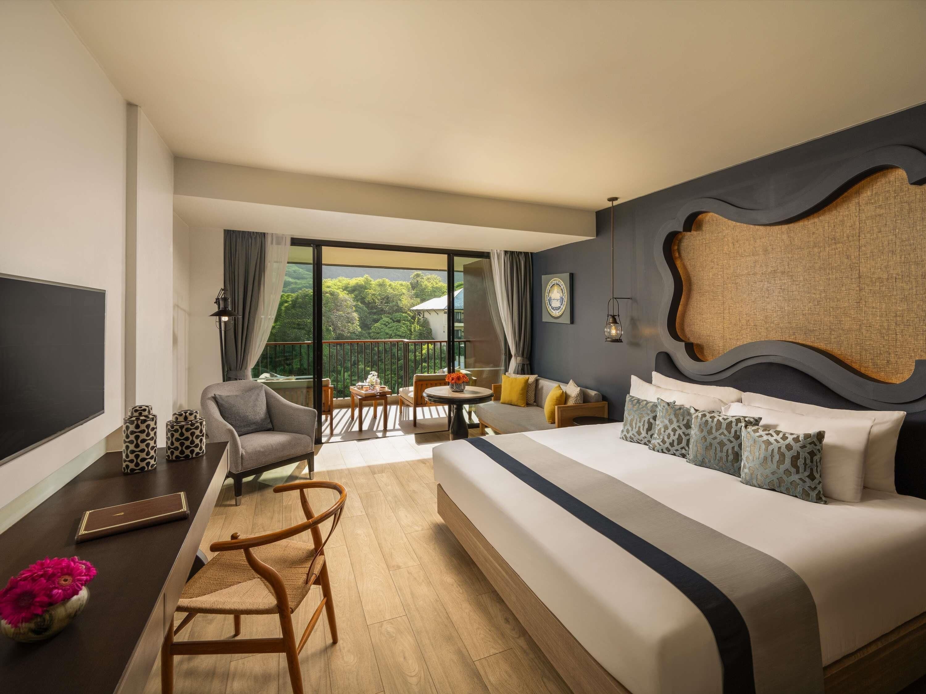 Habitación de hotel con una cama grande, un escritorio, una silla, un sofá y un balcón con vistas.