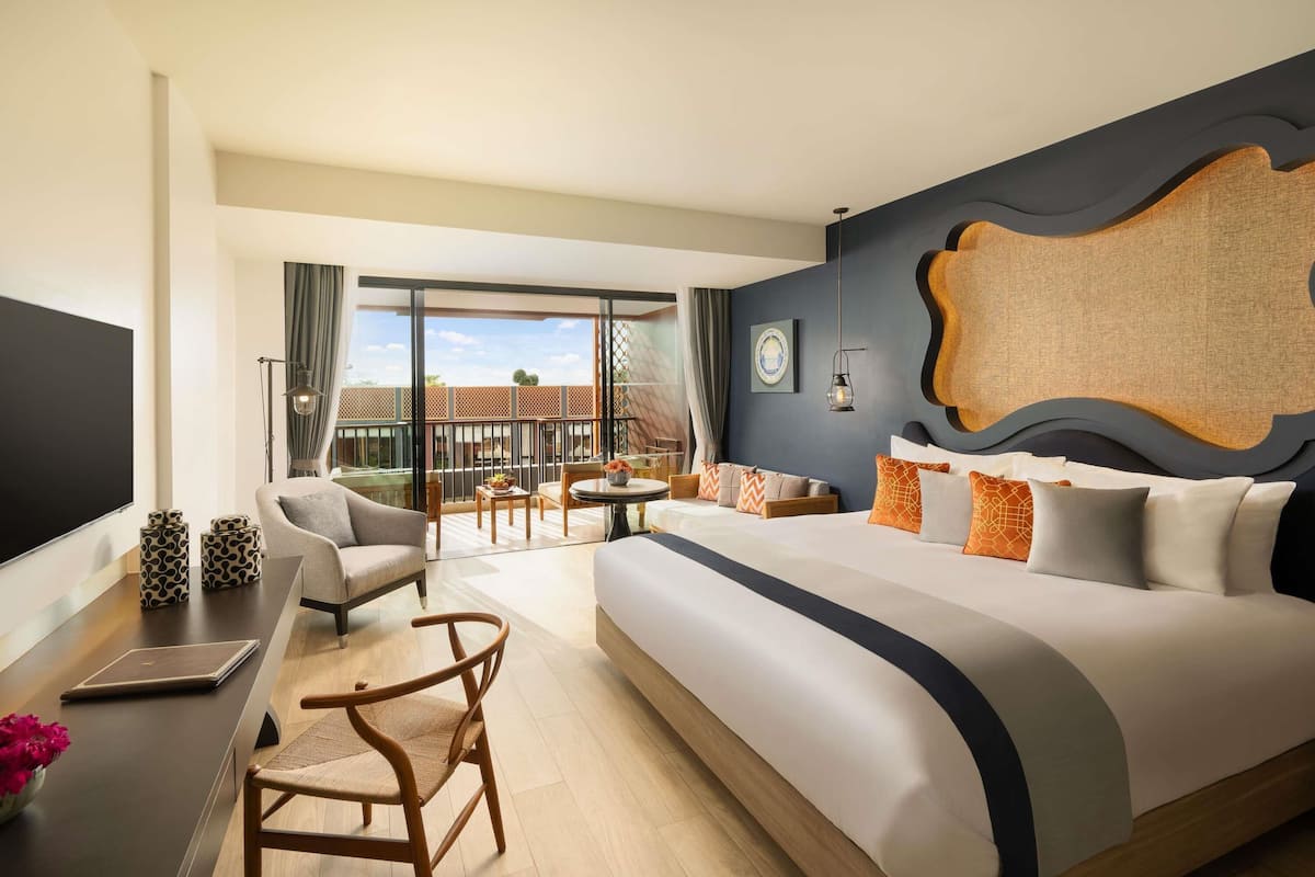 Een hotelkamer met een groot bed, een bureau met een laptop, een stoel, een eettafel met stoelen en een balkon met uitzicht.