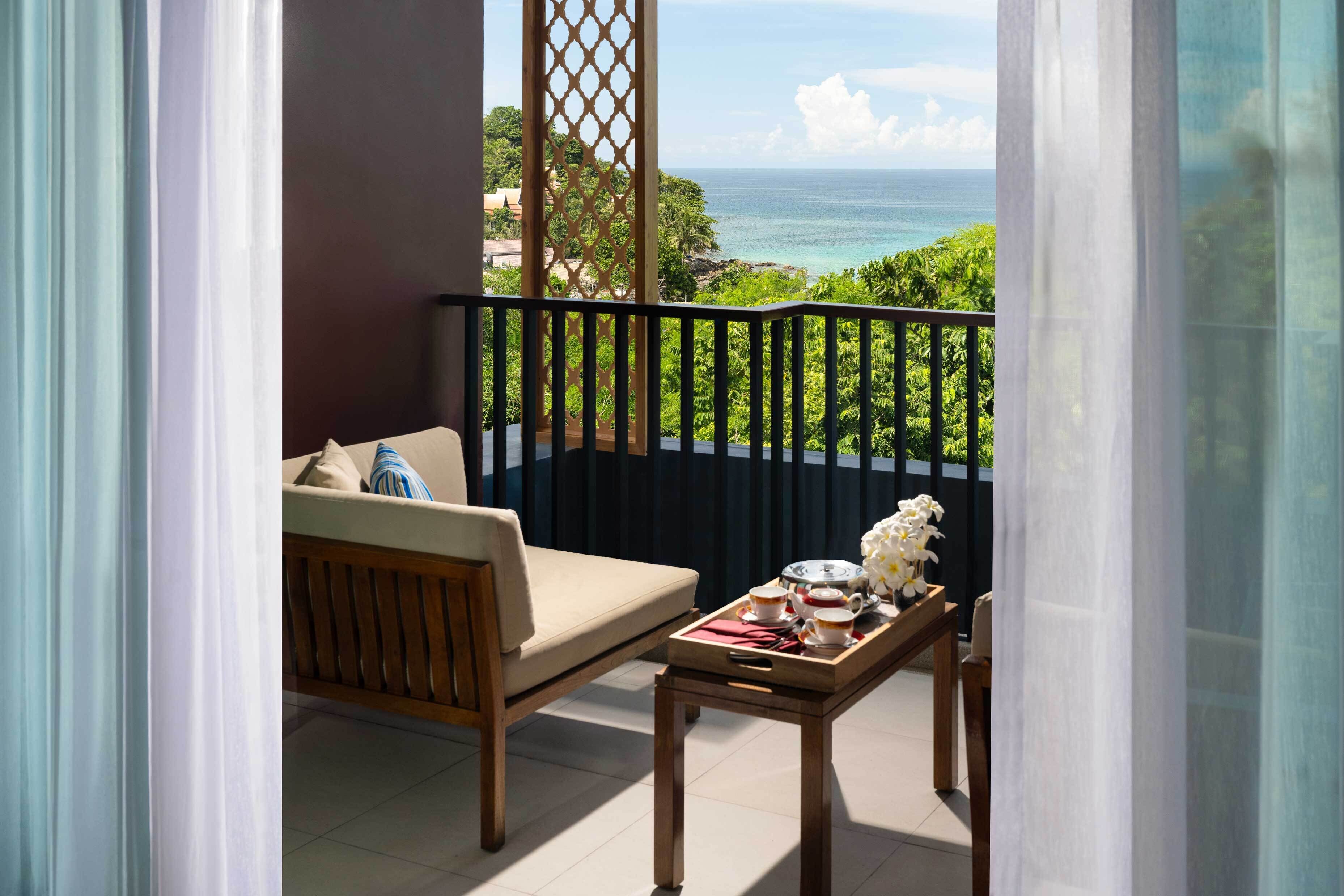 Ein Balkon mit Blick auf das Meer, ein Holzstuhl, ein kleiner Tisch mit Tablett und eine Zierpflanze.