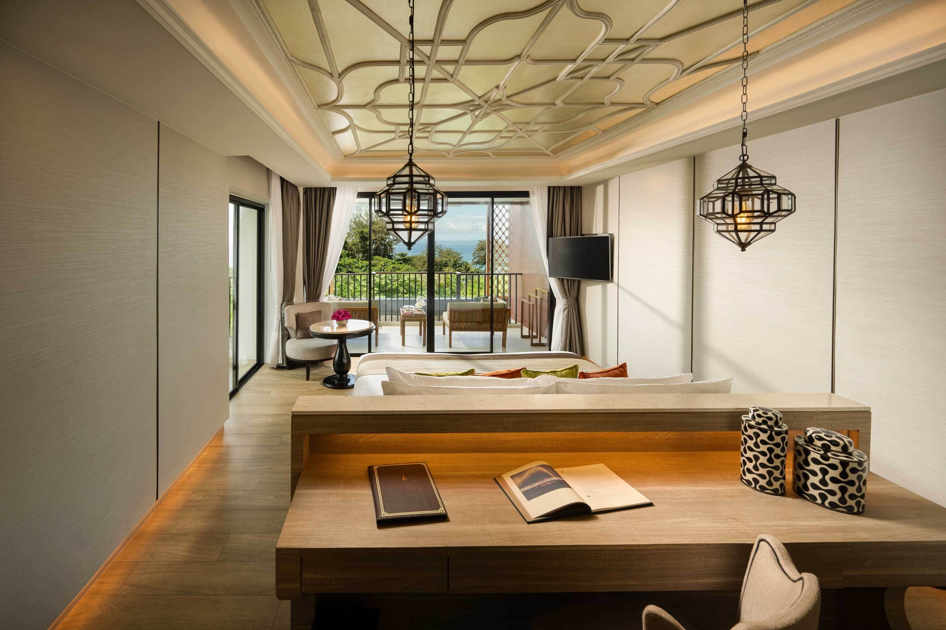 A modern hotel room with a wooden desk, a sofa, and a balcony with a view.