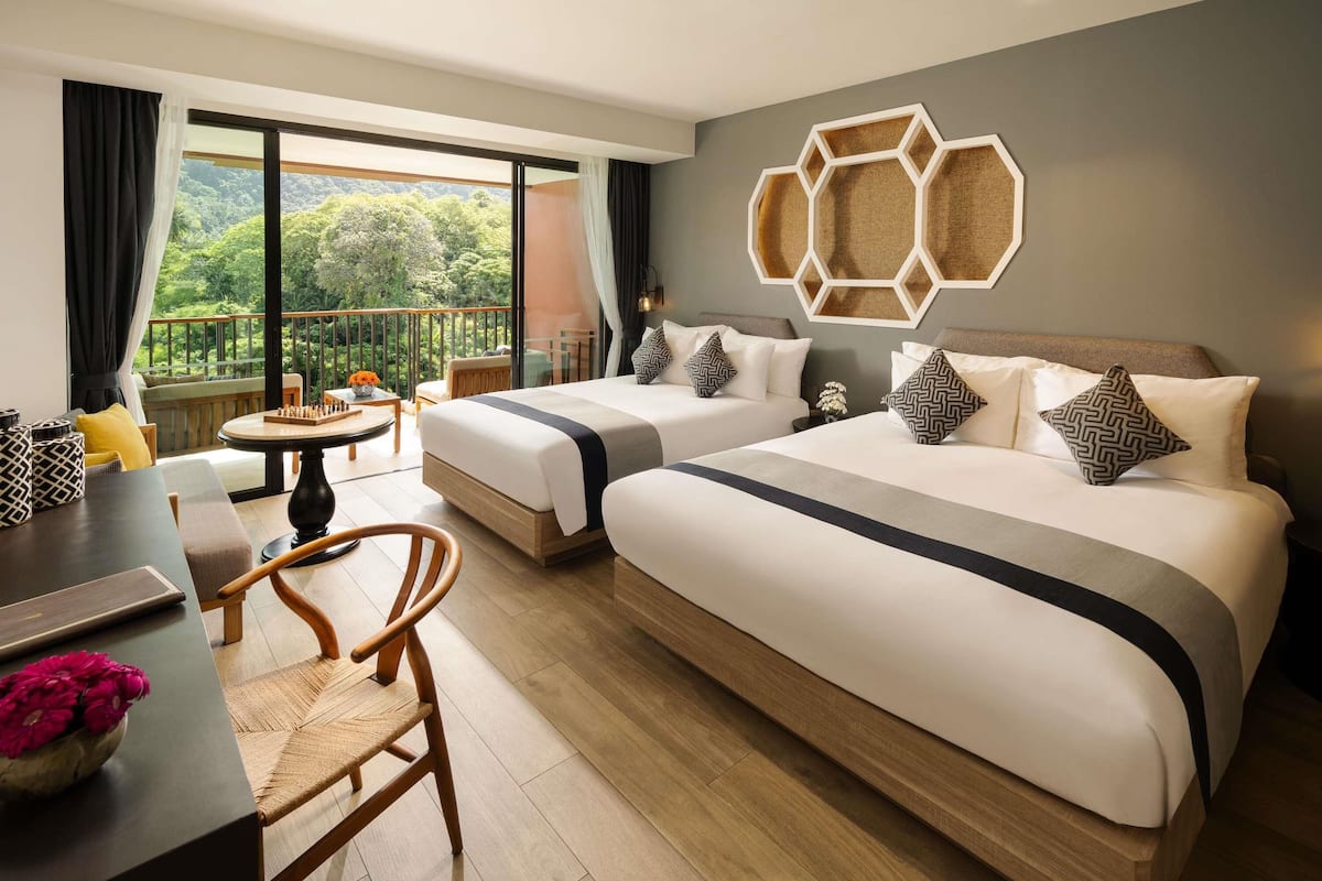 Een hotelkamer met twee bedden, een zithoek en een balkon met uitzicht op het bos.
