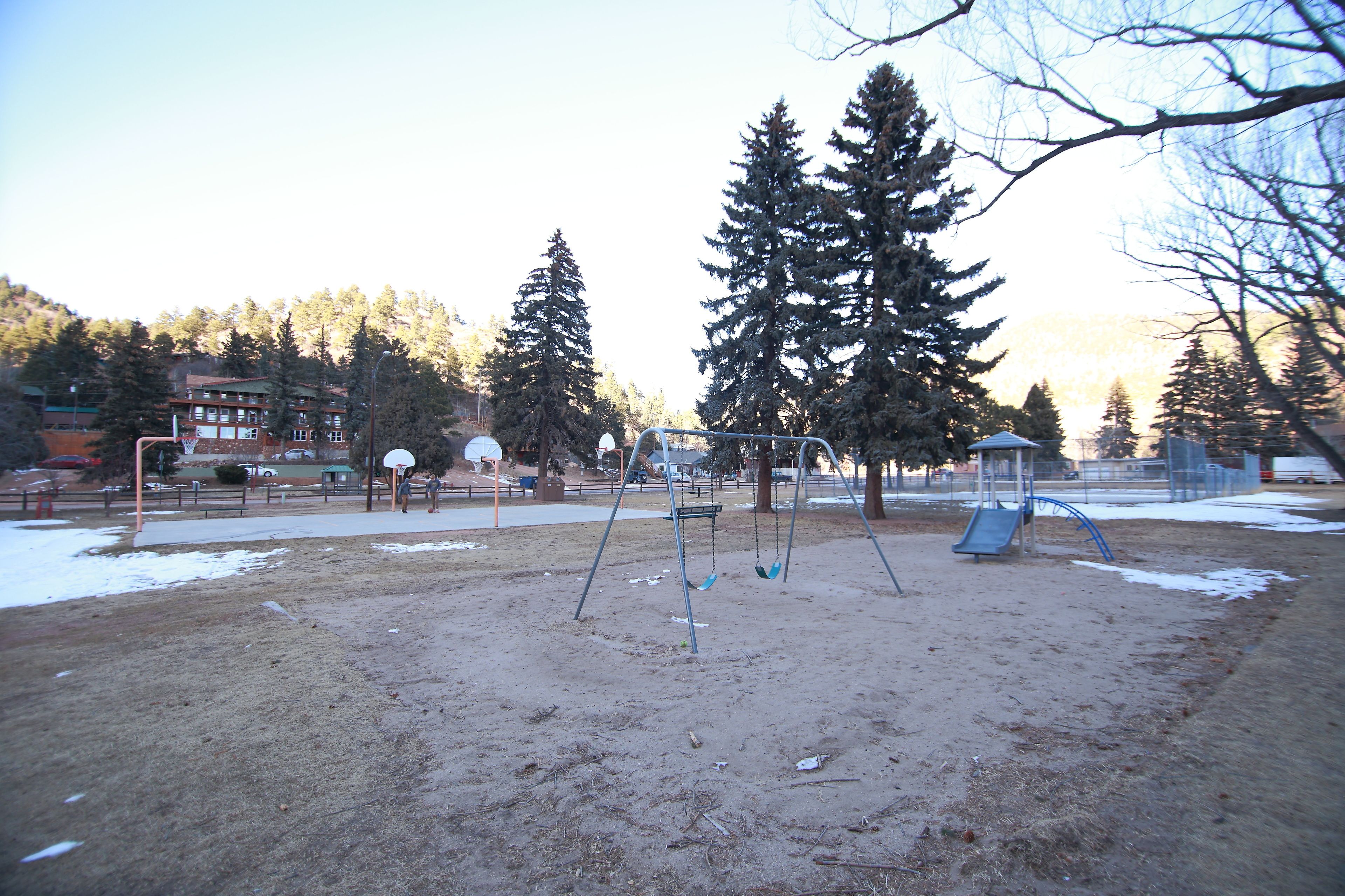 Un terrain de jeux avec des balançoires et un toboggan, entouré d’arbres et d’immeubles.