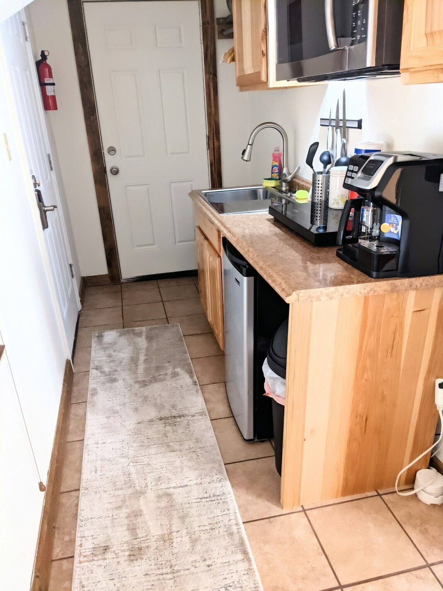 Una cucina compatta con lavello in acciaio inossidabile, macchina da caffè e pensili in legno.