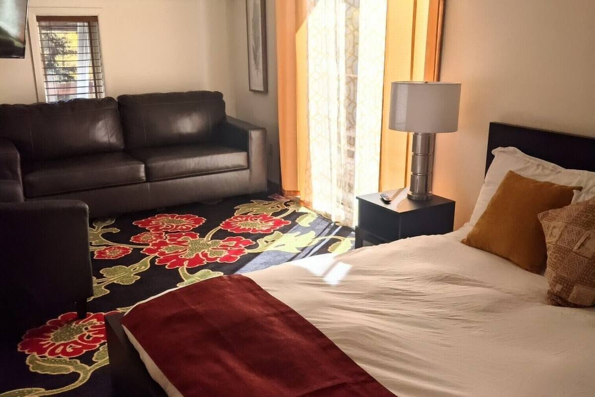 Camera d'albergo con un letto, una poltrona, una lampada e una finestra con tende.