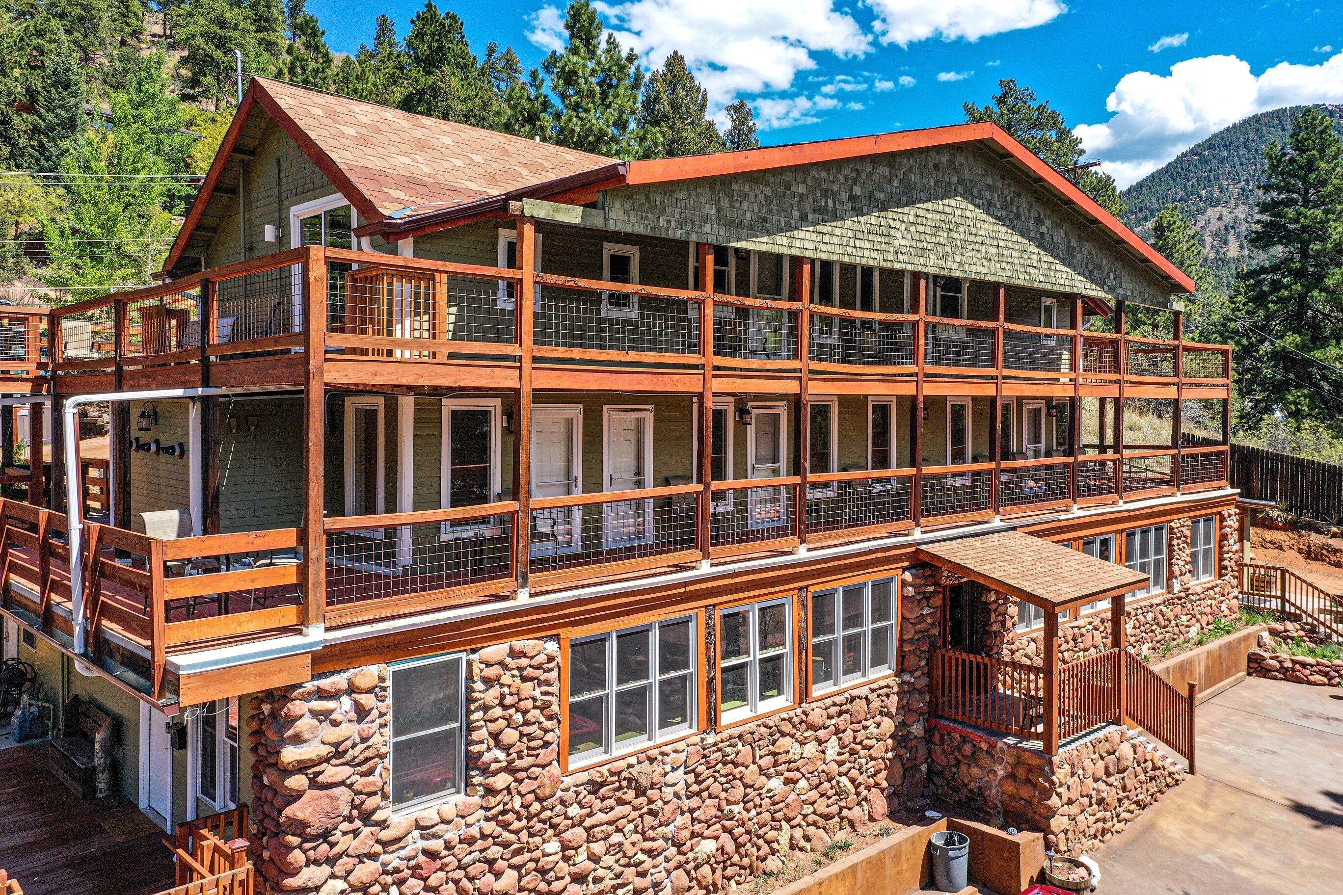 A multi-story lodge with a stone foundation, wooden balconies, and a mountain backdrop.