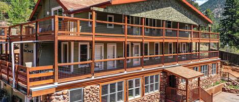 A multi-story lodge with a stone foundation, wooden balconies, and a mountain backdrop.