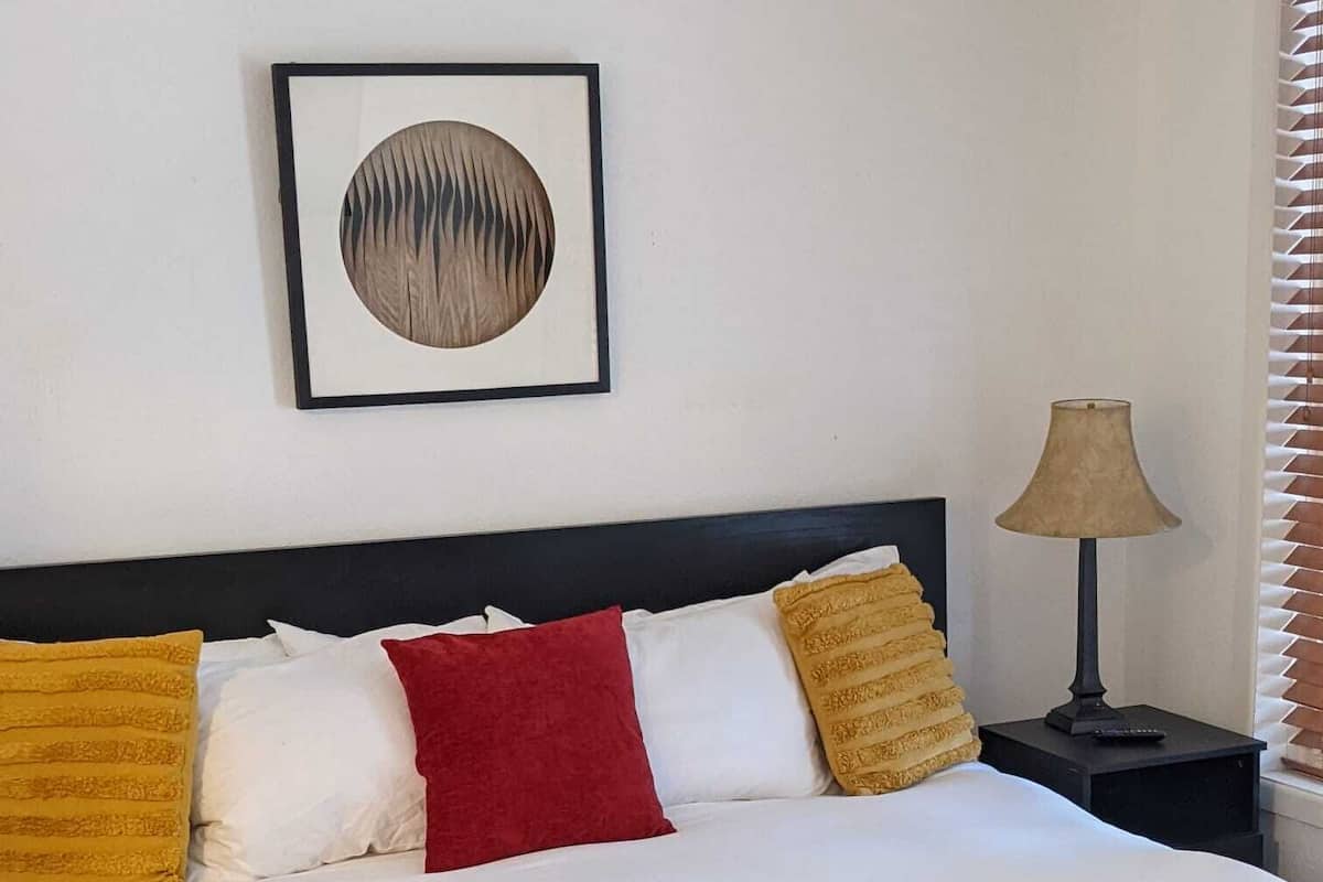 Un letto rifatto con lenzuola bianche e rosse, una coperta rossa e un quadro appeso sopra.