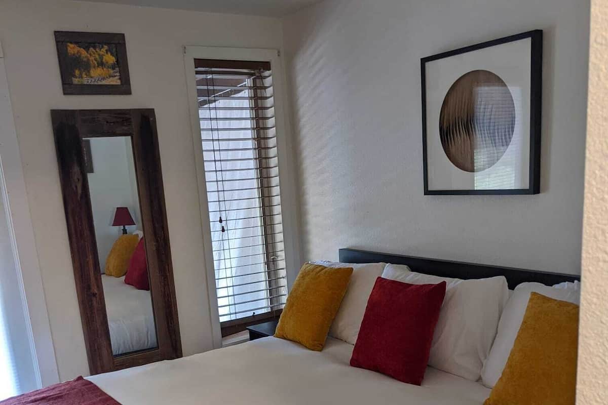 Una camera d'albergo con un letto grande, uno specchio, una finestra con persiane e un quadro appeso al muro.