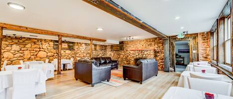 A spacious room with stone walls, wooden beams, and white tables and chairs.