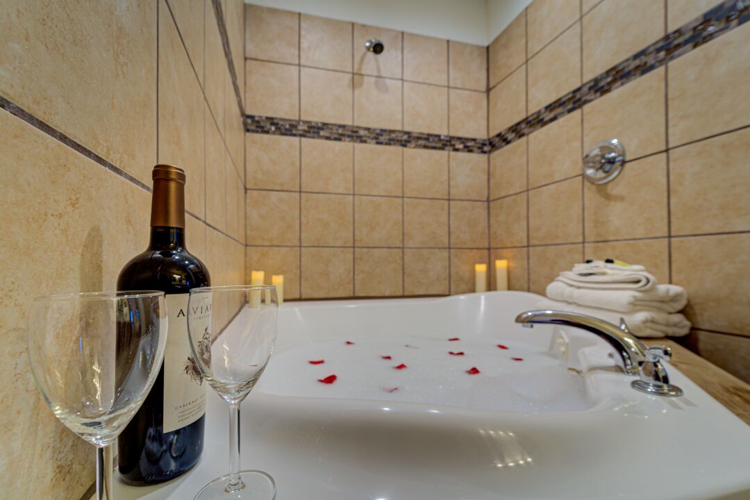 A bathroom with a bathtub, a wine bottle, and two glasses on a counter.