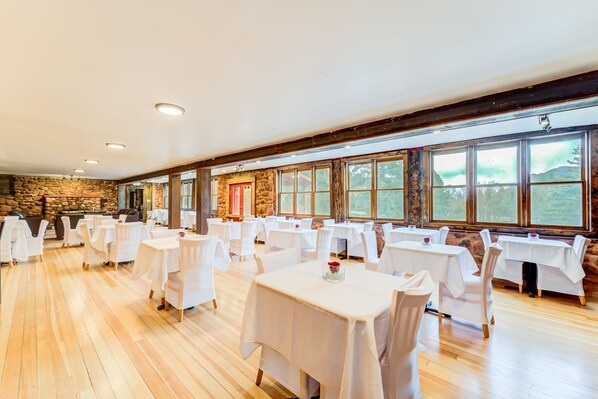 A spacious dining area with multiple tables and chairs, large windows with a view of the outdoors, and a stone wall. - The Green Mountain Falls Lodge (Green Mountain Falls)