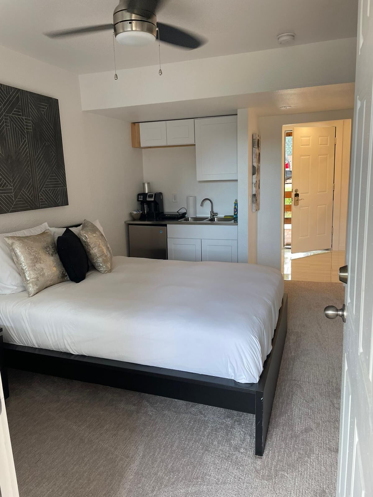 Ein Schlafzimmer mit Bett, Deckenventilator, Küchenzeile und einer Badezimmertür.