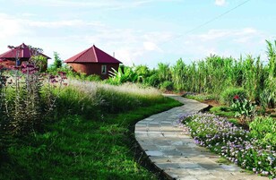 Um caminho leva a um edifício com telhado vermelho, cercado por vegetação exuberante e plantas floridas.
