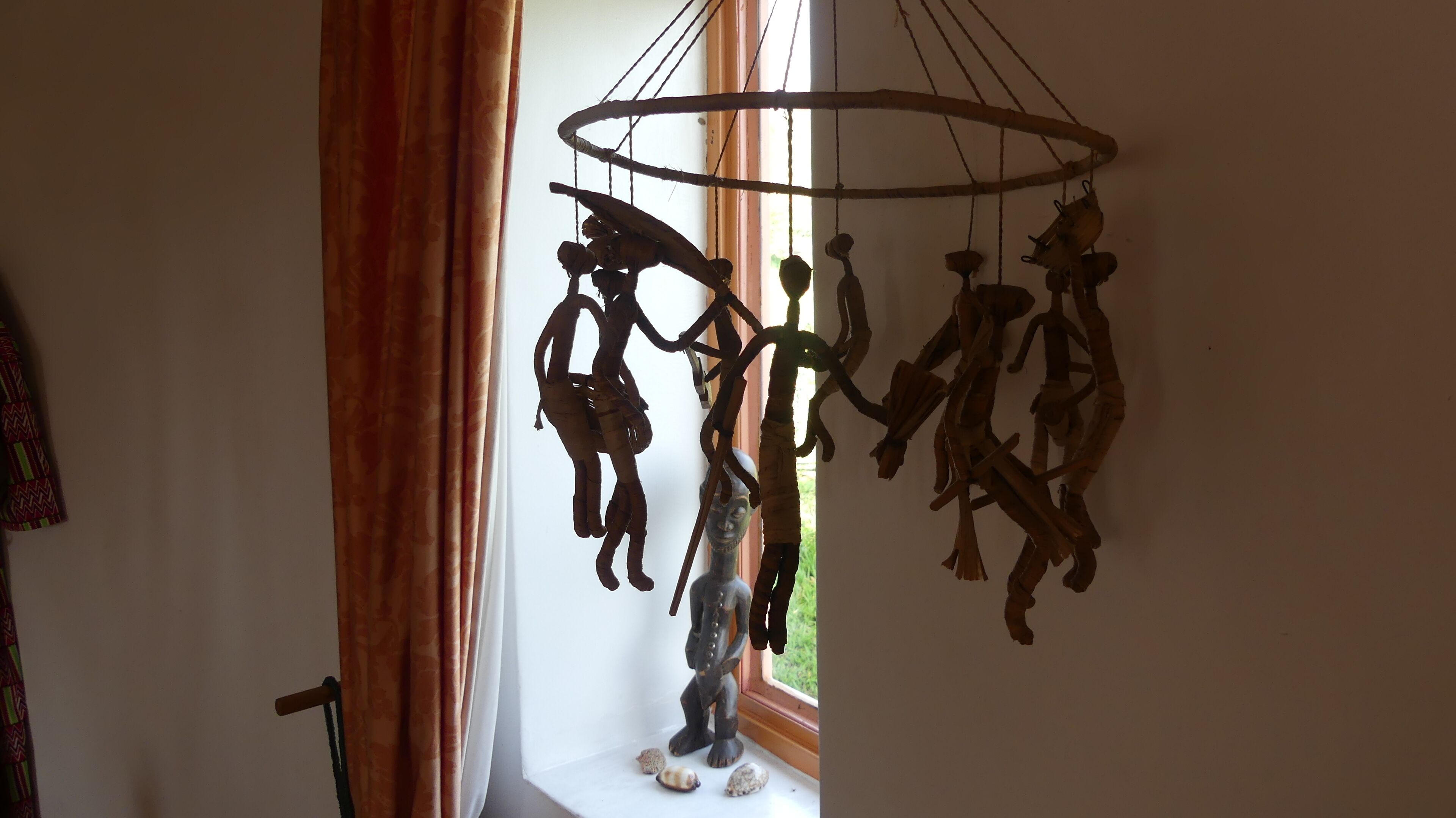 Une pièce avec une fenêtre, un rideau et une sculpture en bois suspendue.