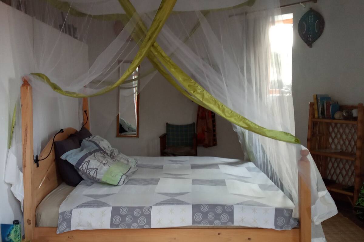 A bed with a canopy, a bedside table, a bookshelf, and a mirror on the wall.