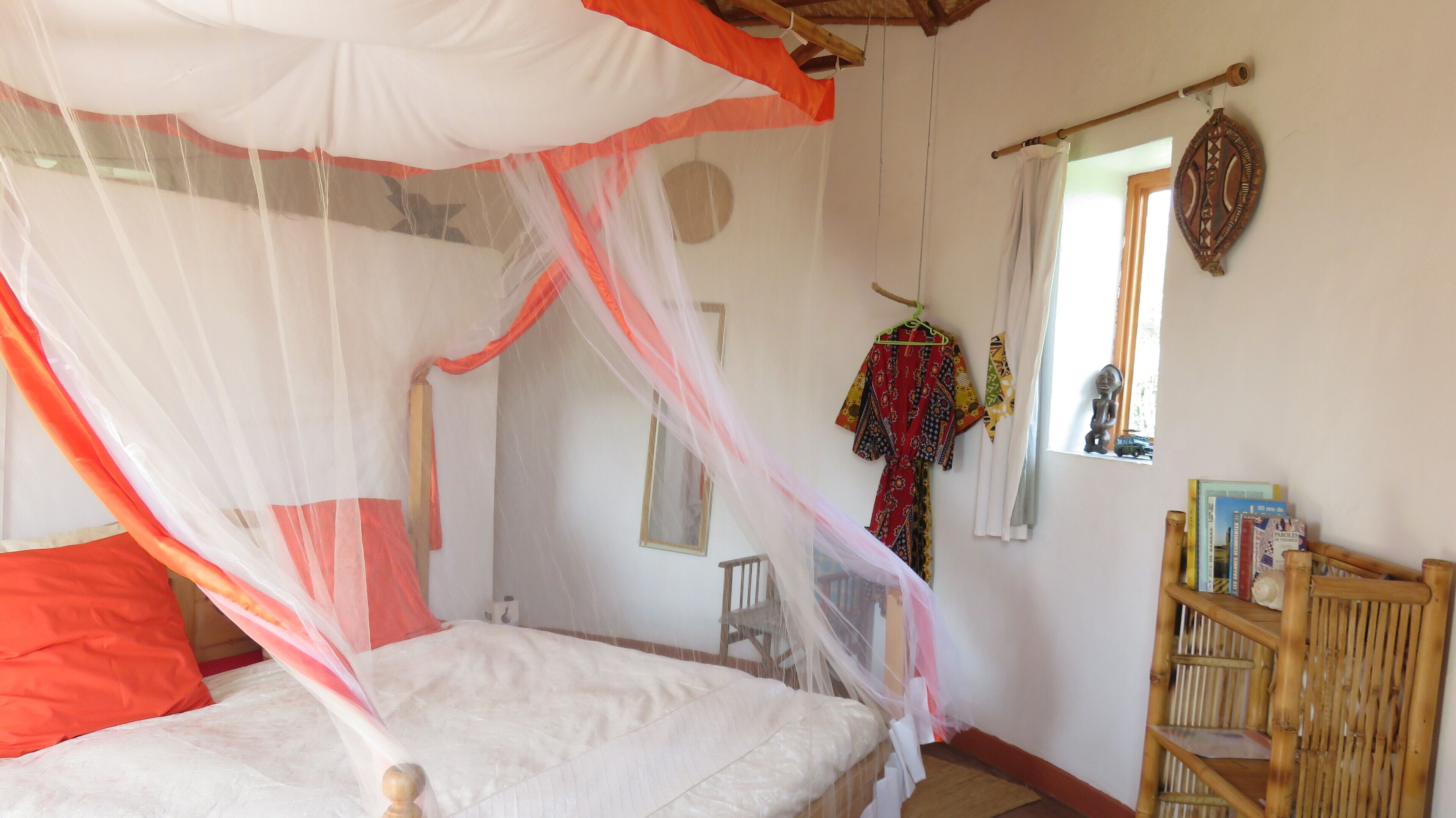 A room with a bed under a canopy, a wooden chair, a small table, and a wall with a mirror and a decorative item.