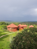 Paisagem rural com edifícios de telhado vermelho, área gramada e vista distante de colinas.