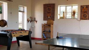 A room with a foosball table, ping pong table, and a shelf with decorative items. - Bugesera Lodge (Ntarama)