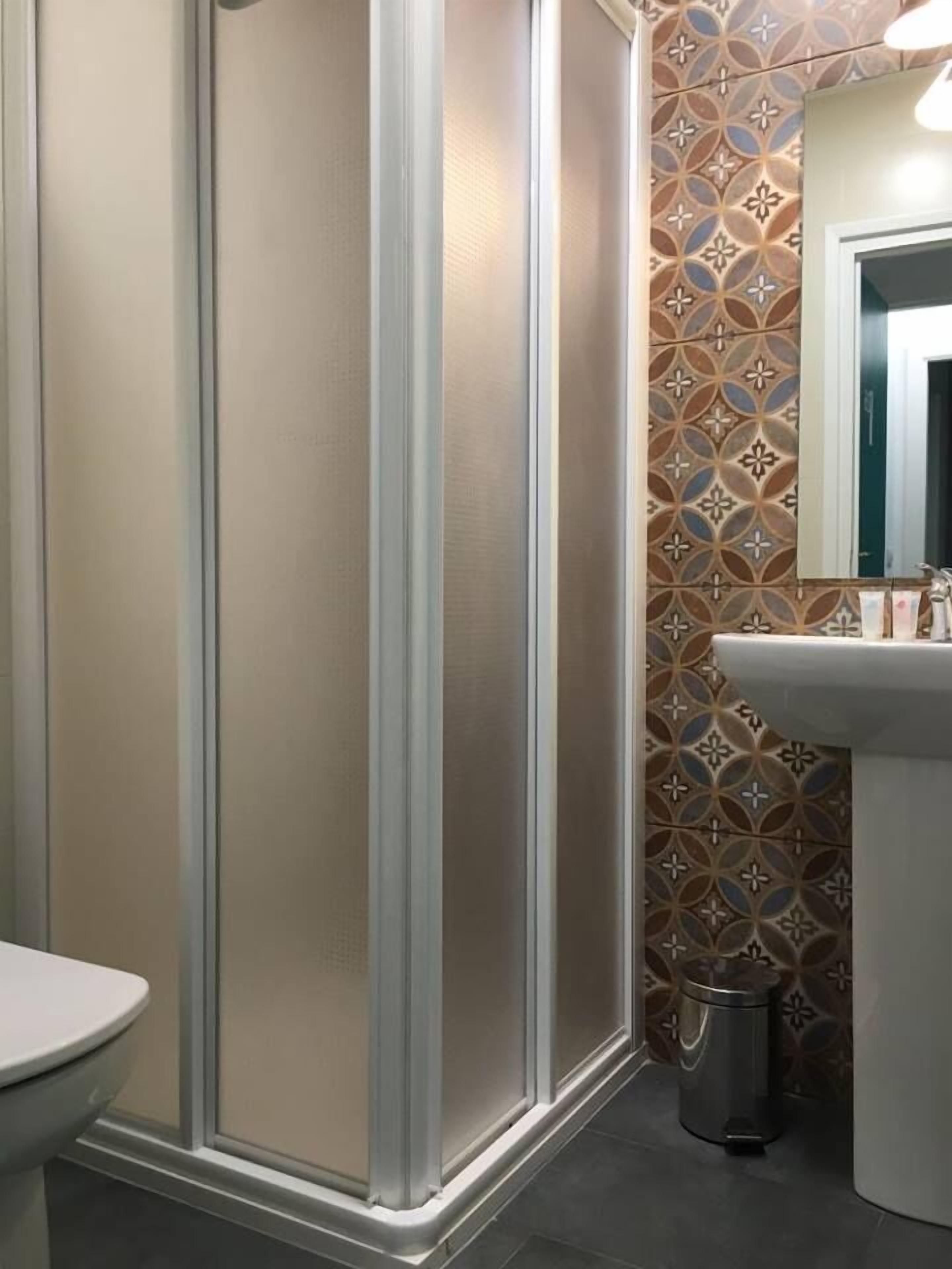 A bathroom with a toilet, a sink, a shower enclosure, and a trash can.