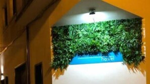 A hallway with a sign for a hostel, a green wall with foliage, and a tiled floor. - Room Concept Hostel (Santo Domingo de la Calzada)