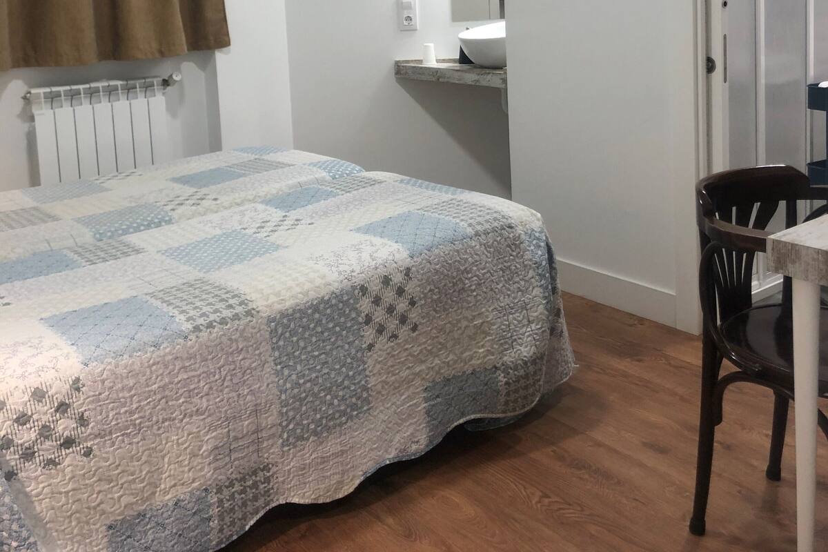 A bedroom with a bed, a chair, a radiator, a mirror, and a door.