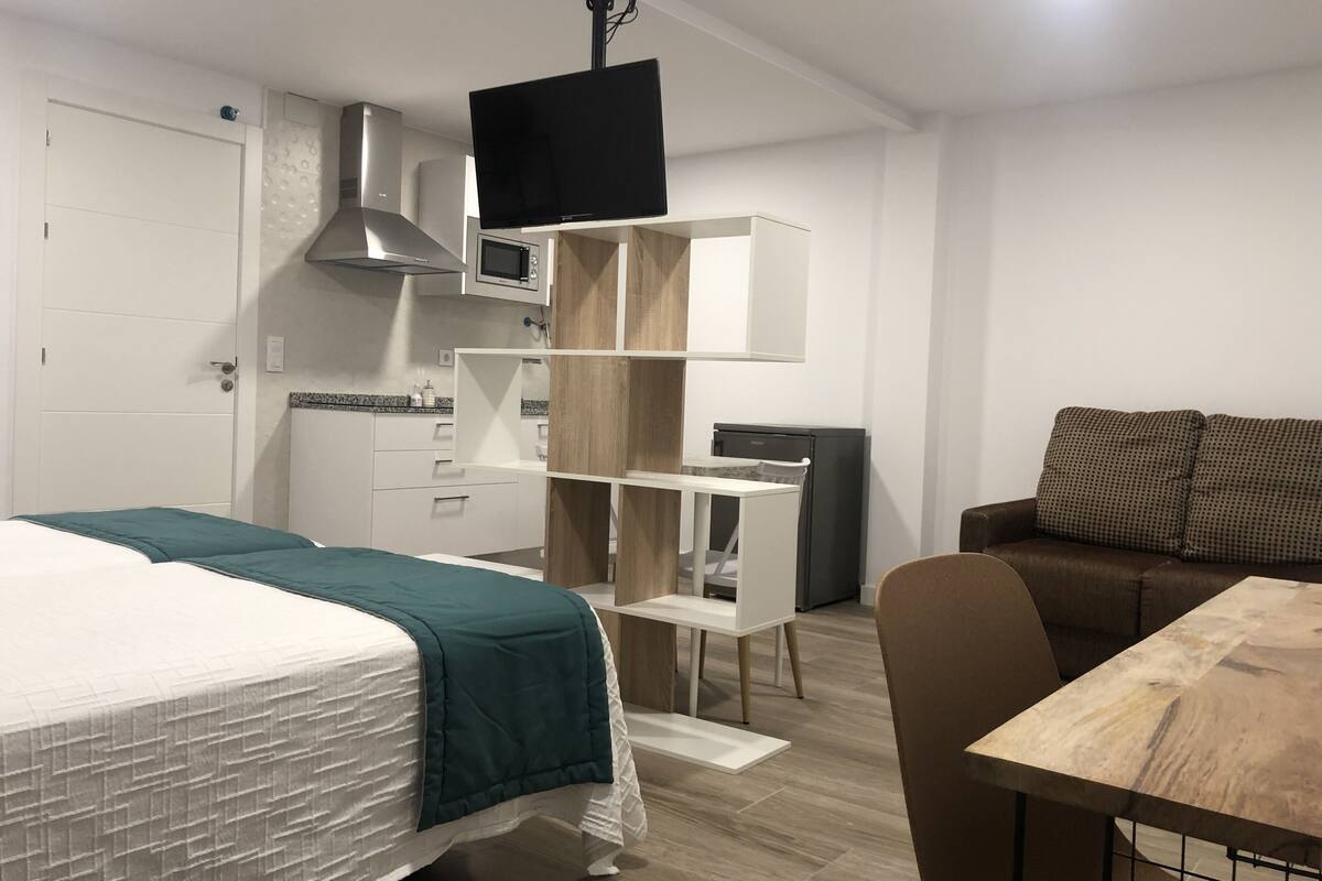 A modern hotel room with a bed, a desk, a chair, a television, and a sofa.