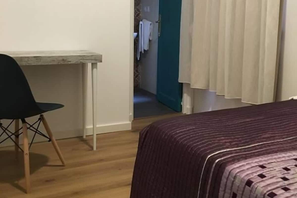 A bedroom with a bed, a desk, and a chair. There is a door leading to another room.