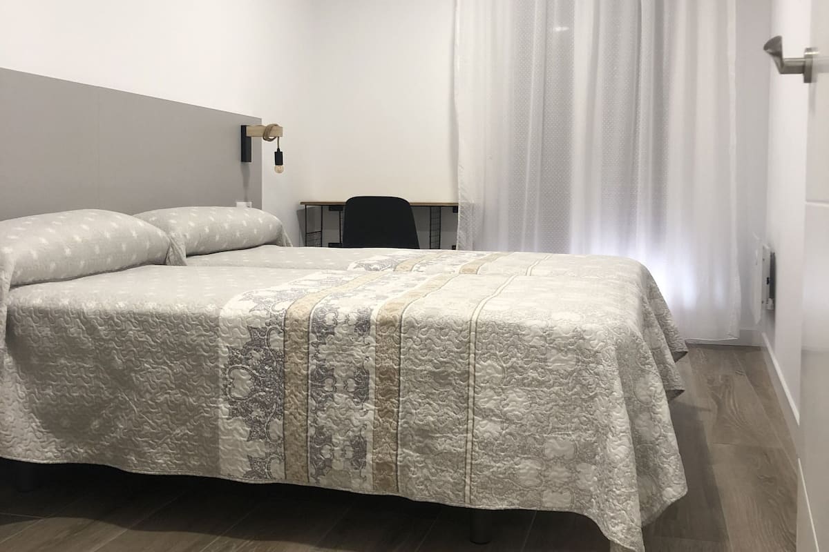 A hotel room with a bed, a desk, a chair, and a TV mounted on the wall.