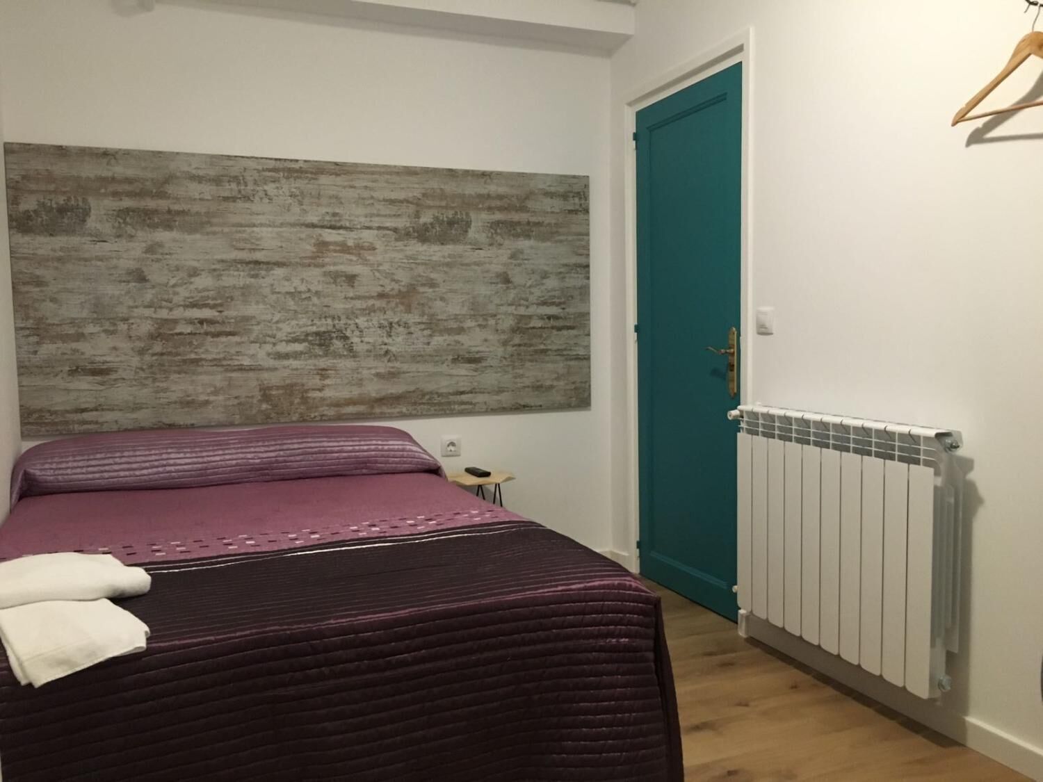 Quarto com cama, porta verde-água, radiador e piso de madeira.