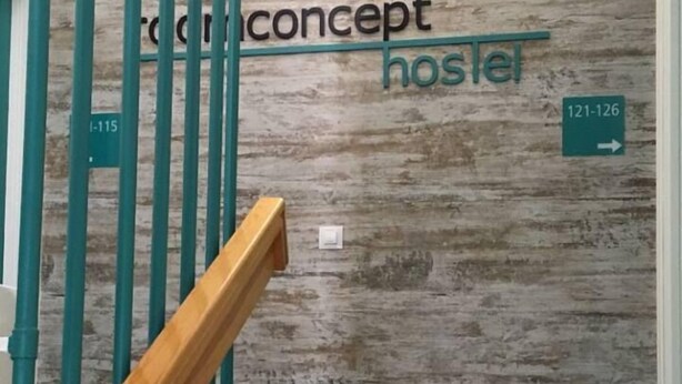A staircase with teal railings leading to a wall with a wooden texture. The wall has a sign that reads "Concept Hostel" and a directional sign pointing to room numbers 121-126. - Room Concept Hostel (Santo Domingo de la Calzada)