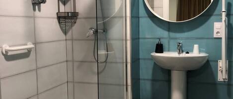 A modern bathroom with a glass-enclosed shower, a pedestal sink, and a round mirror.