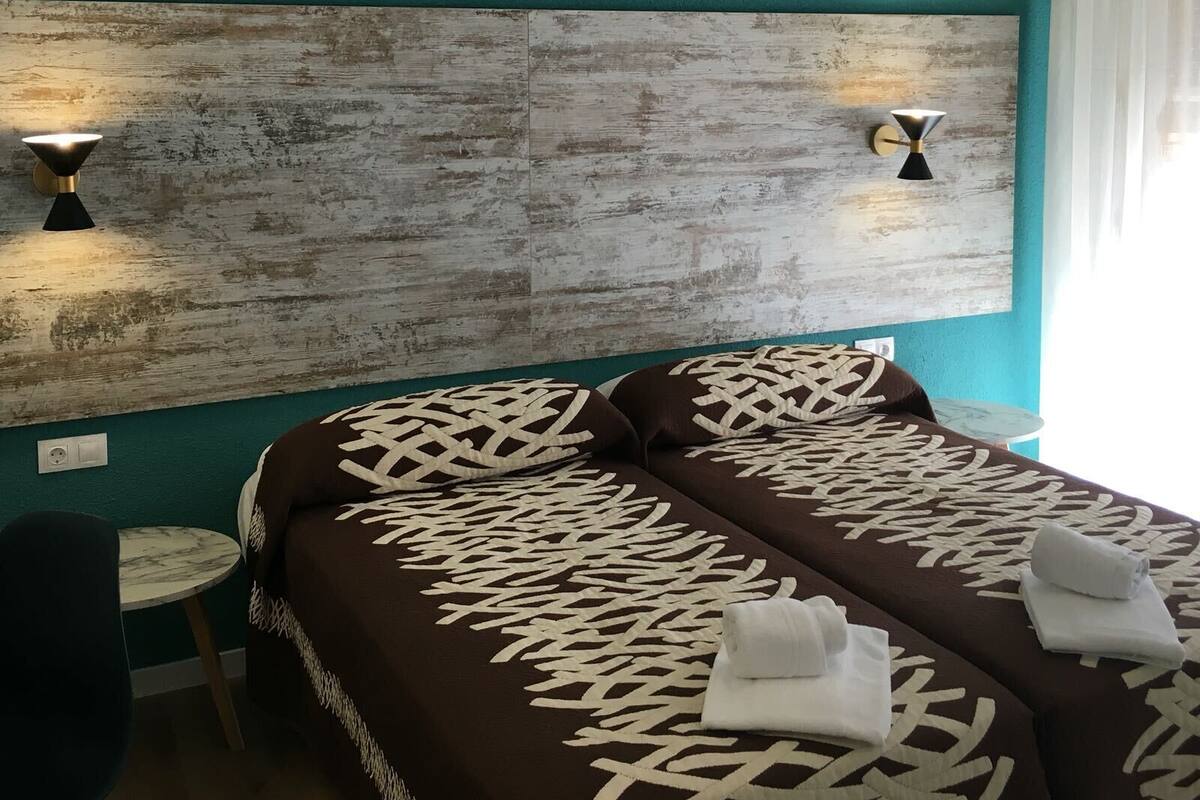 A hotel room with teal walls, a wooden headboard, two bedside tables, and a bed with patterned bedding.