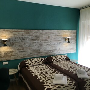 A hotel room with teal walls, a wooden headboard, two bedside tables, and a bed with patterned bedding. - Room Concept Hostel (Santo Domingo de la Calzada)