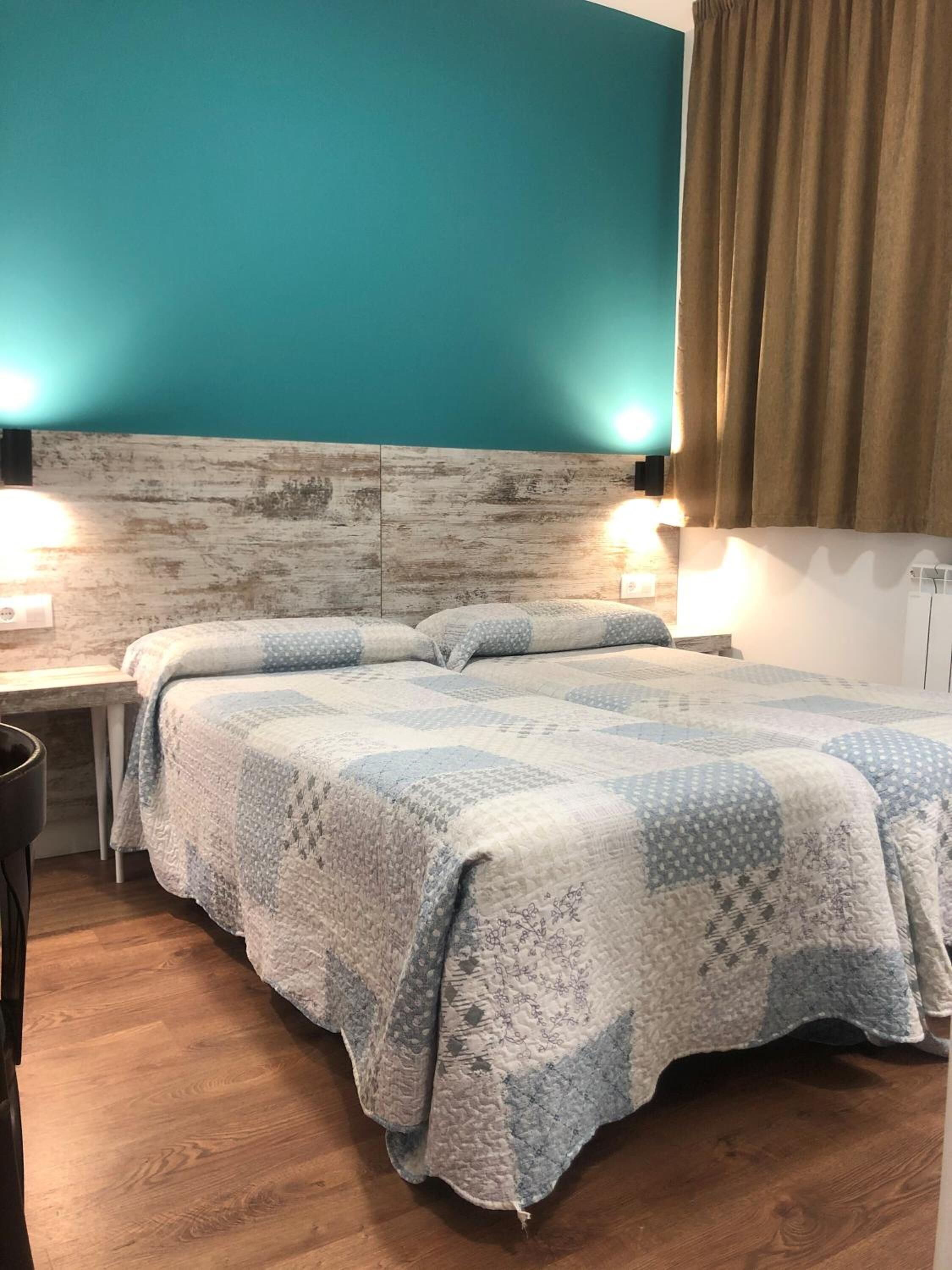 A bedroom with a wooden headboard, a bed with a quilt, bedside lamps, and a curtain.