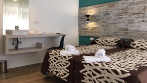 A modern hotel room with a teal accent wall, a wooden headboard, and a large bed with patterned bedding. A vanity with a mirror and a sink is visible, along with a small trash bin. - Room Concept Hostel (Santo Domingo de la Calzada)