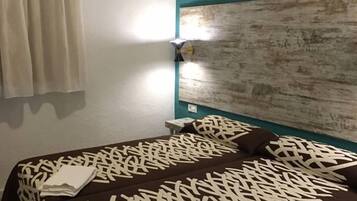 A double bed with a patterned bedspread, a teal accent wall, and a window with a curtain.