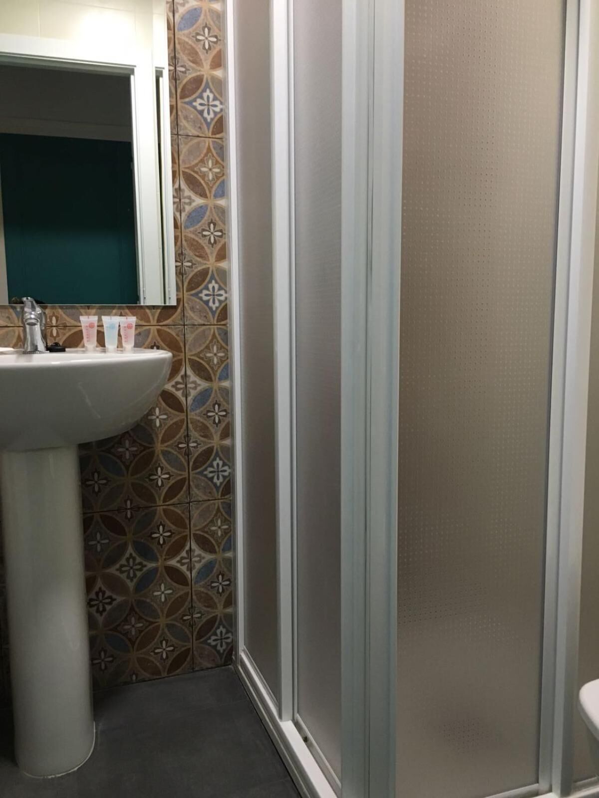 Un baño con un lavamanos blanco, un espejo encima y baldosas estampadas en las paredes.