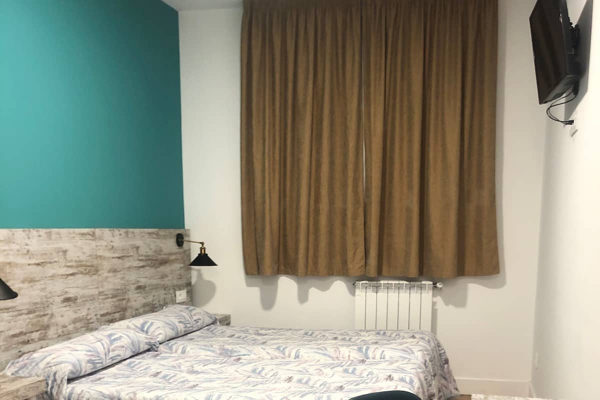 A room with a bed, a desk, a chair, a radiator, and a TV mounted on the wall.