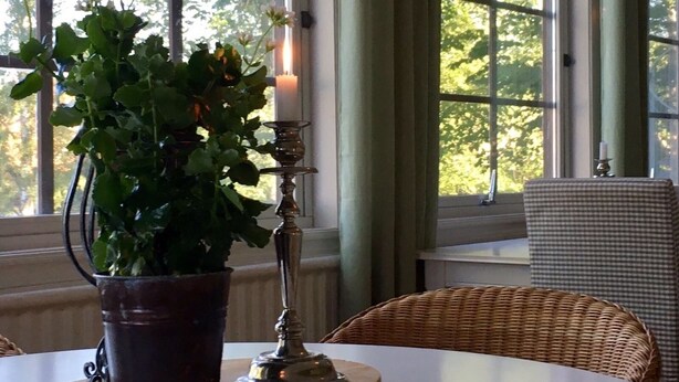 A room with a table, a potted plant, a candle holder, and a wicker chair.