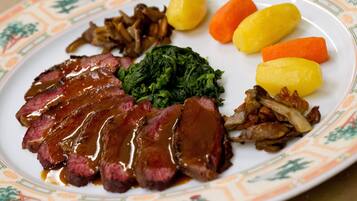 A plate of food with sliced meat, potatoes, carrots, and greens.