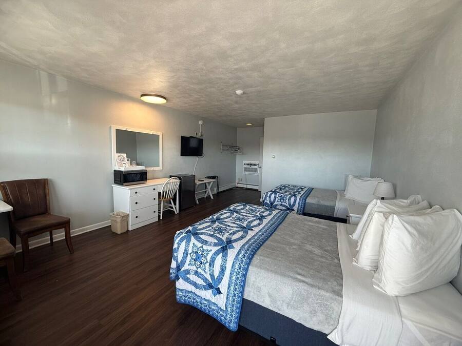 Habitación de hotel con dos camas, un escritorio, una silla, un televisor y una kitchenette pequeña.