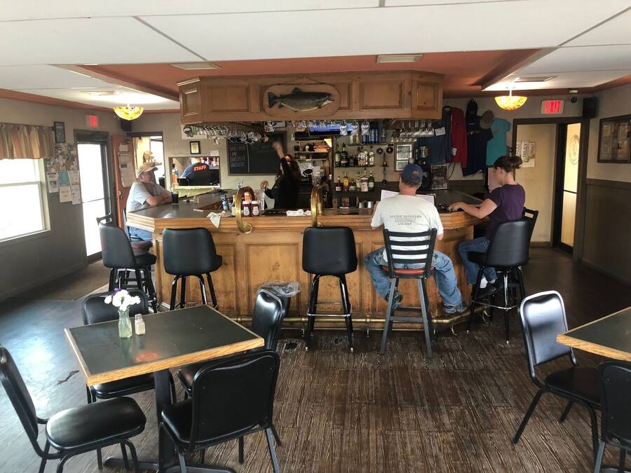 A bar area with wooden bar counter, black chairs, and a fish mounted on the wall.
